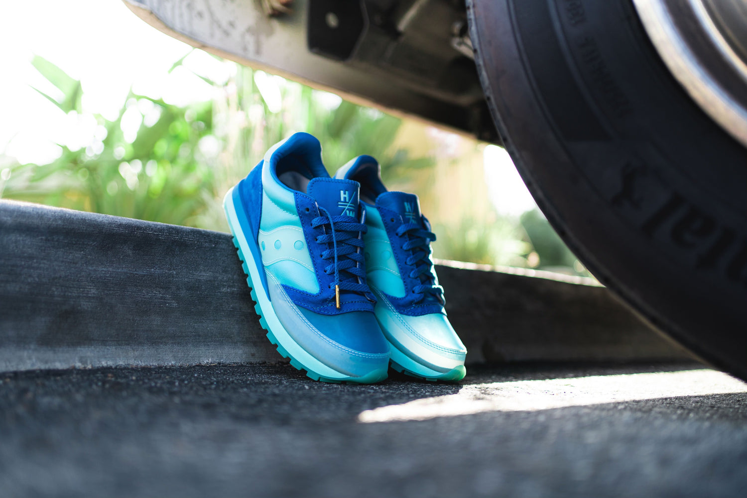 A pair of blue sneakers standing next to a curb under a car