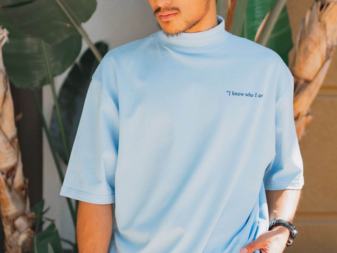 A man wearing a blue t shirt in front of a potted plant