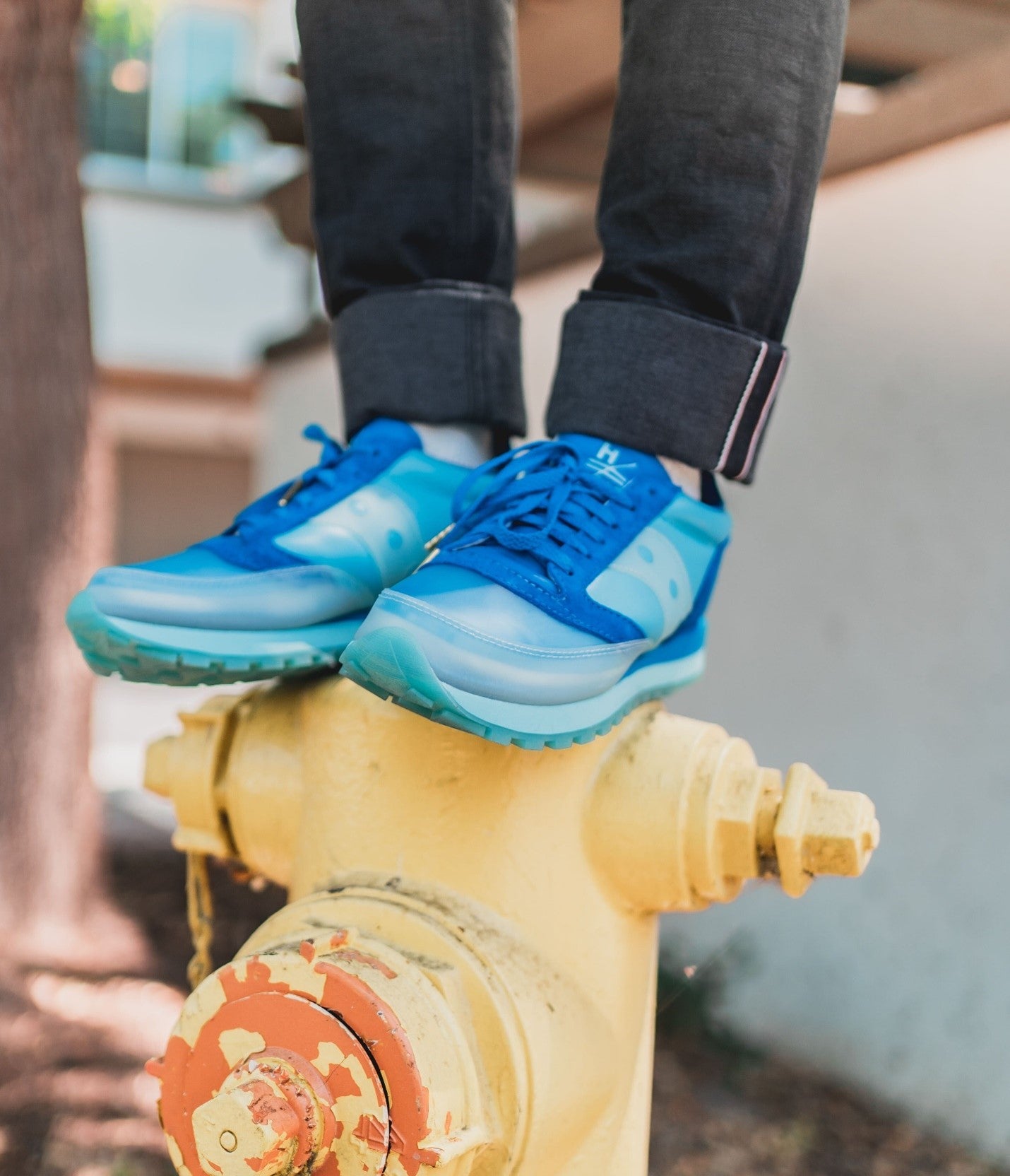 A person standing on a yellow fire hydrant wearing a pair of blue sneakers