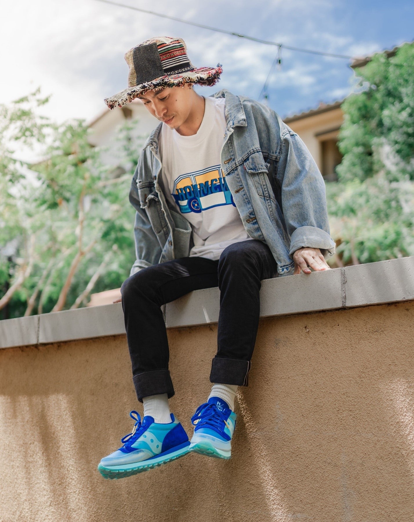 A man wearing a white shirt and black jeans sitting on a ledge looking down