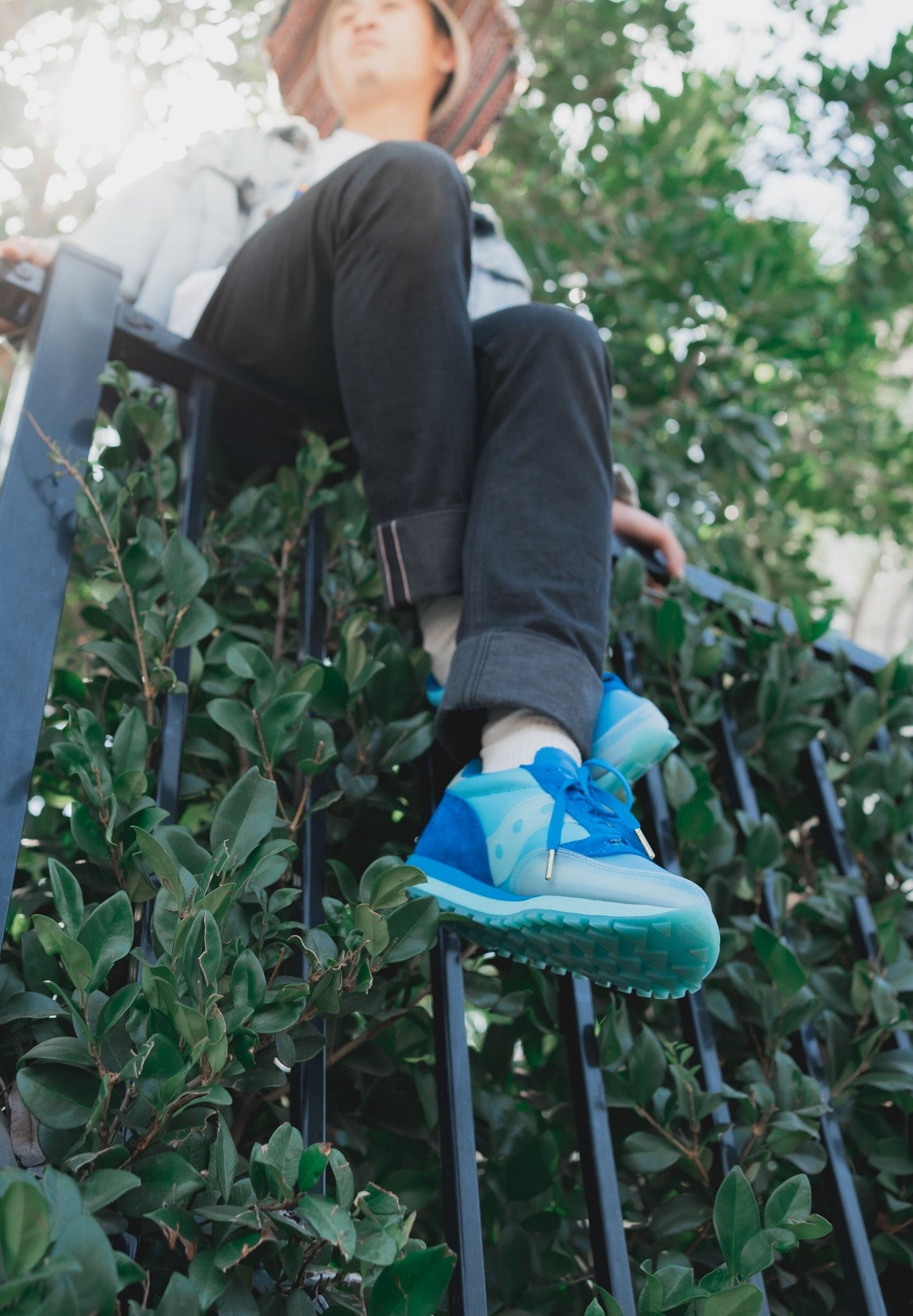 A man sitting on a black fence wearing black jeans and a pair of blue sneakers